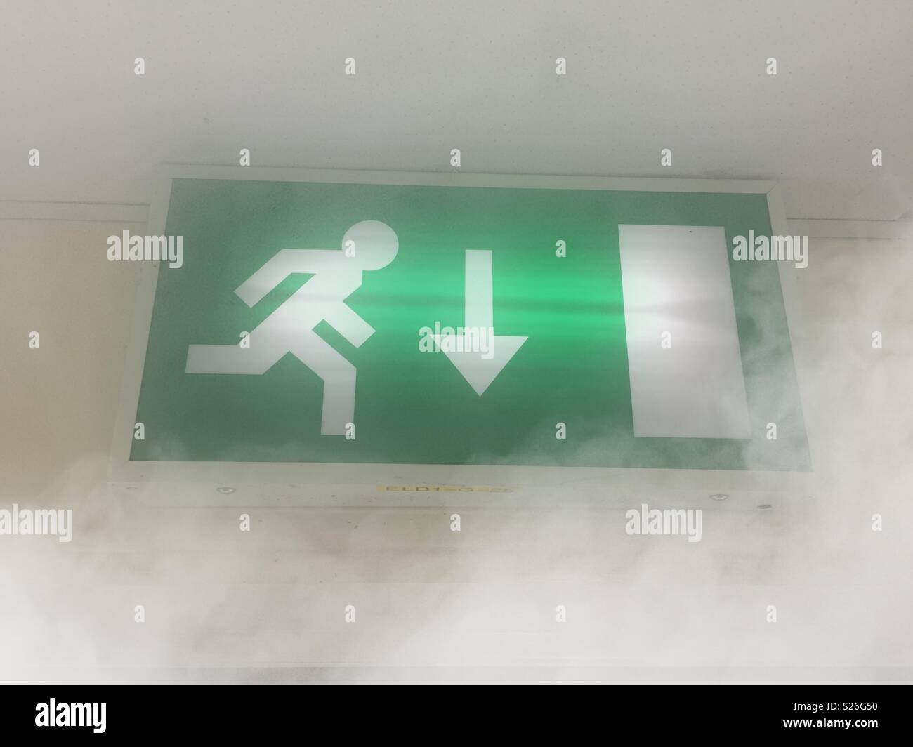 Green illuminated fire escape sign above doorway, about to be engulfed by smoke. Where there's smoke there's fire - Smartphone Captured Stock Image