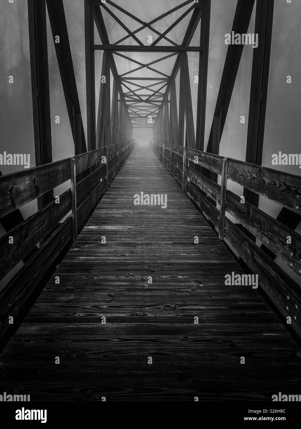 A spooky or haunting black and white of a view across a truss footbridge in a dark foggy morning at Tims Ford State Park in Winchester Tennessee. Stock Photo
