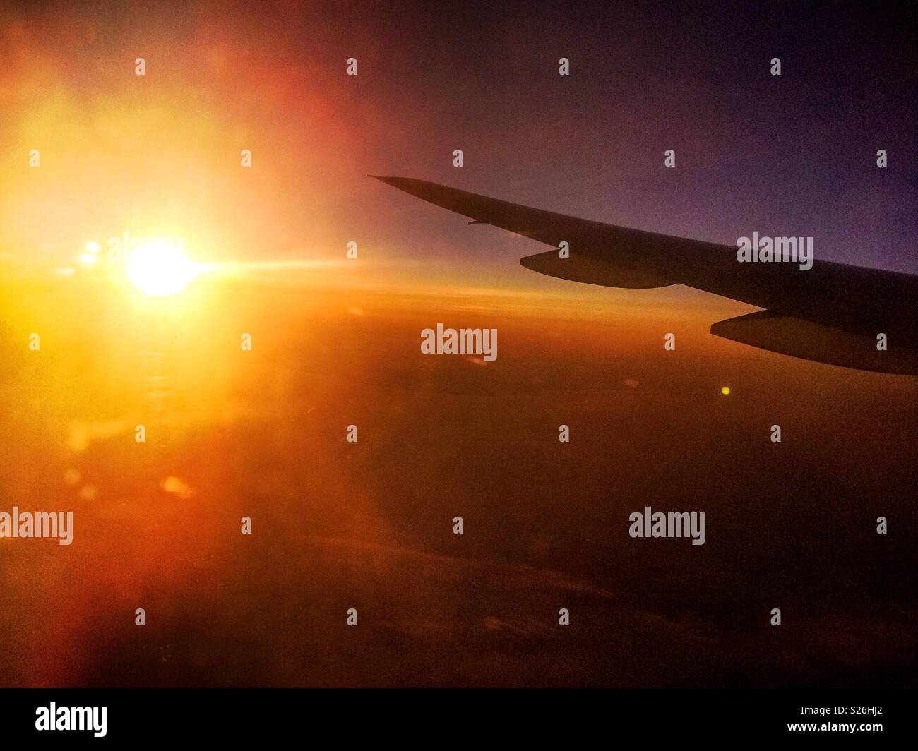 Flying above the clouds during sunset. Shot taken through an airplane window with one of its the wing in the foreground. - Smartphone Captured Stock Image