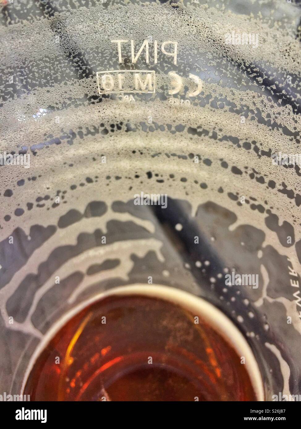 View from inside a nearly empty beer glass, on a pub garden table, showing residual froth rings as the beer has been drunk. The word PINT is shown in reverse on the side of the glass. - Smartphone Captured Stock Image