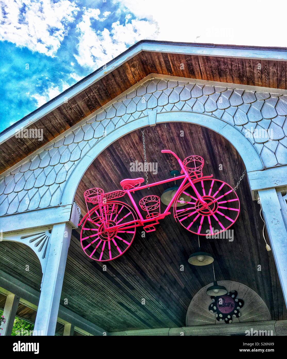 Pink bicycle hanging over store entrance with blue sky and clouds above Stock Photo