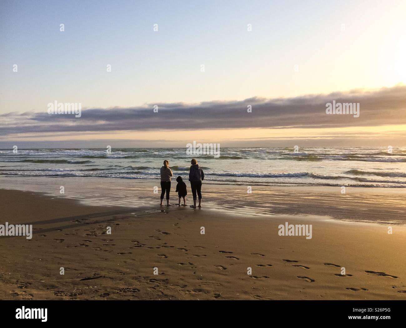 Looking at the ocean. Three people admiring the pacific ocean on late afternoon before sunset in Cannon Beach, Oregon Coast, USA. - Smartphone Captured Stock Image