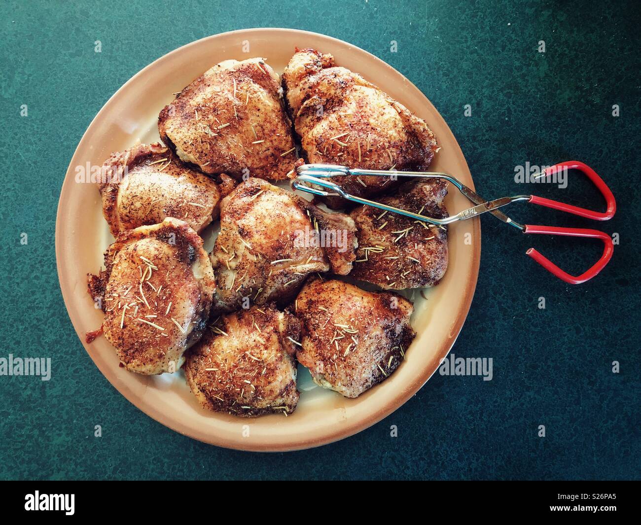 Oven roasted, herb crusted chicken thighs on a plate with tongs Stock Photo