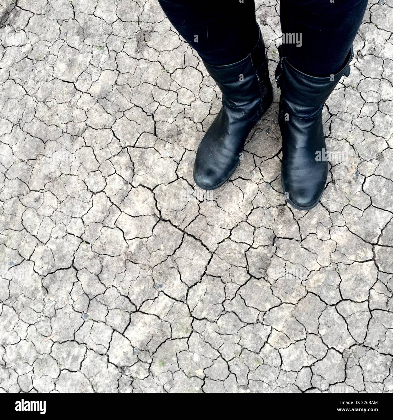 Person wearing black jeans and black boots standing on dry cracked earth - Smartphone Captured Stock Image