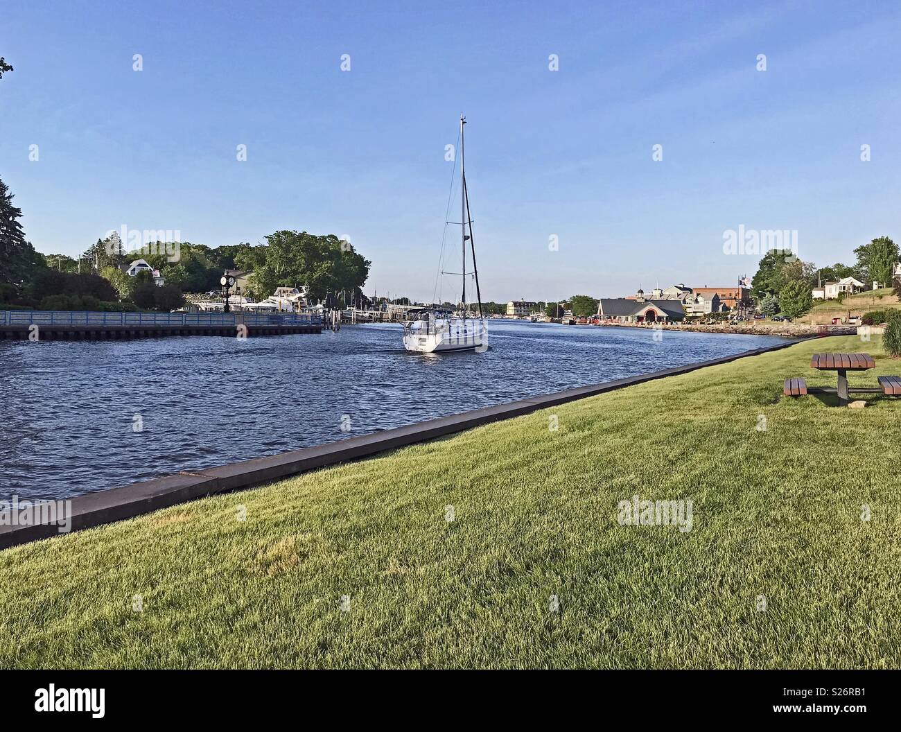 South Haven, Michigan, USA – June 8, 2018:  A sailboat traveling up the black river towards the harbor in South Haven, Michigan, USA off of Lake Michigan with blue sky copy space. Stock Photo