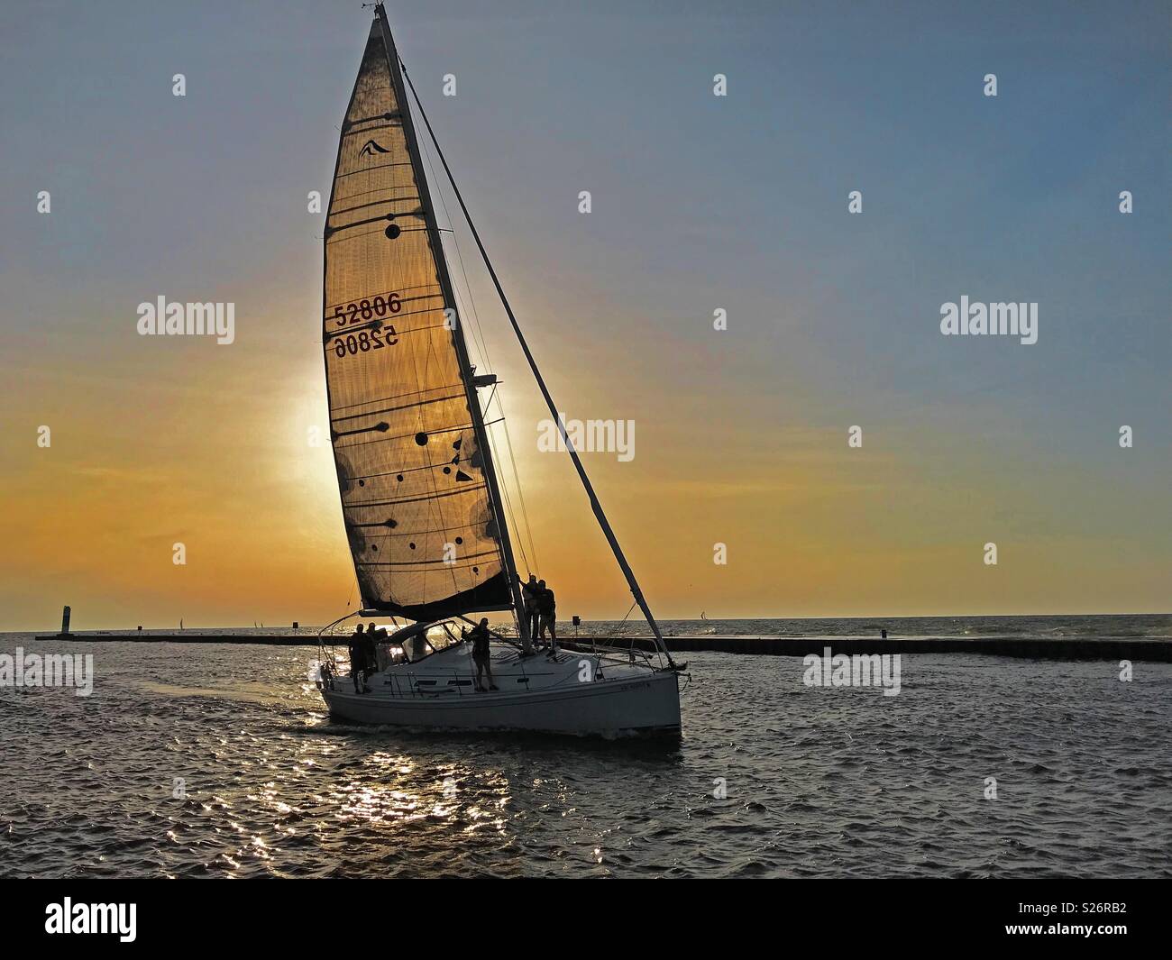South Haven, Michigan, USA – June 8, 2018:  A sailboat at sunset traveling up the black river from Lake Michigan towards the harbor in South Haven, Michigan, USA with blue sky copy space. - Smartphone Captured Stock Image
