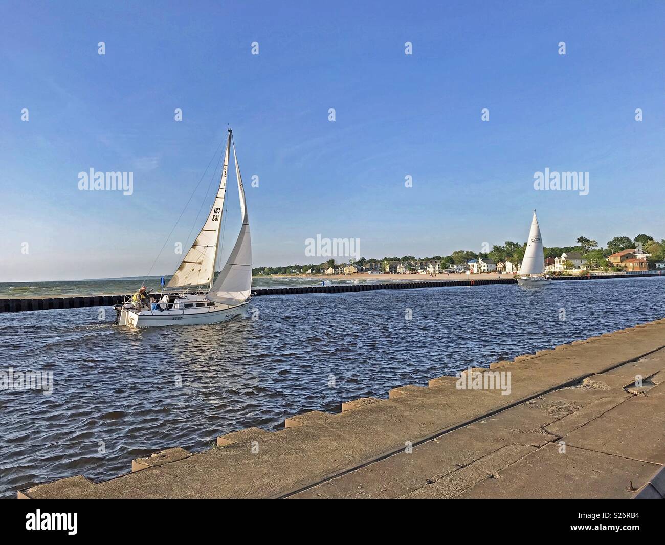 South Haven, Michigan, USA – June 8, 2018:  Two sailboats traveling up the black river from Lake Michigan towards the harbor in South Haven, Michigan, USA with blue sky copy space. - Smartphone Captured Stock Image