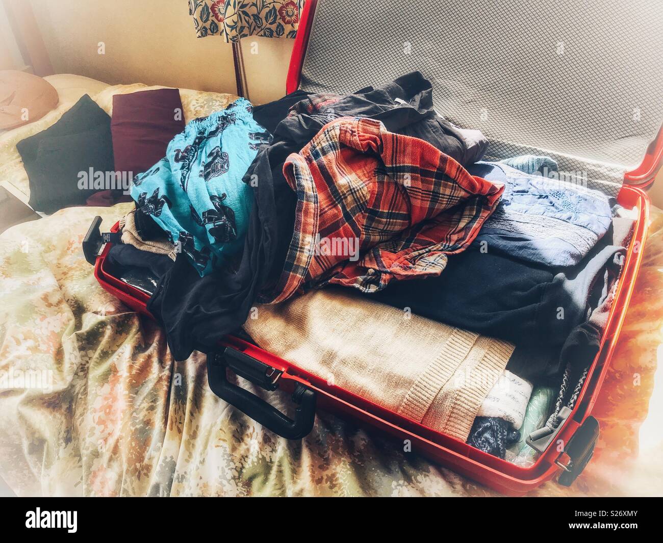 Open suitcase, full of clothes, on a bed Stock Photo