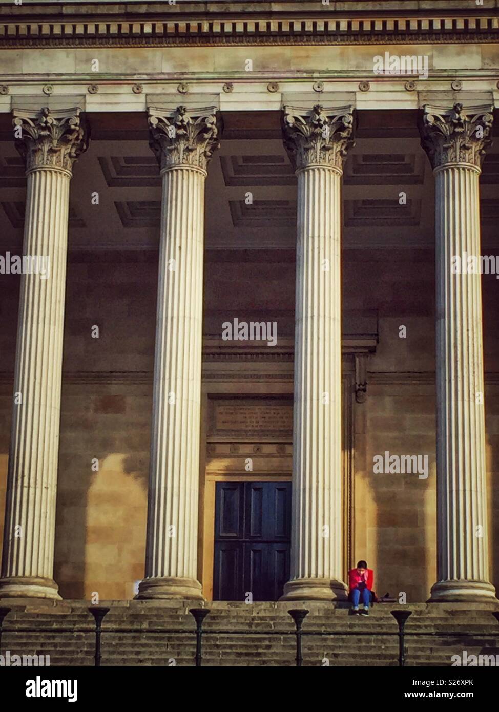 London, U.K. A lone student sits and reads beneath the impressive columns of UCL. One of the world's most prestigious medical universities. - Smartphone Captured Stock Image
