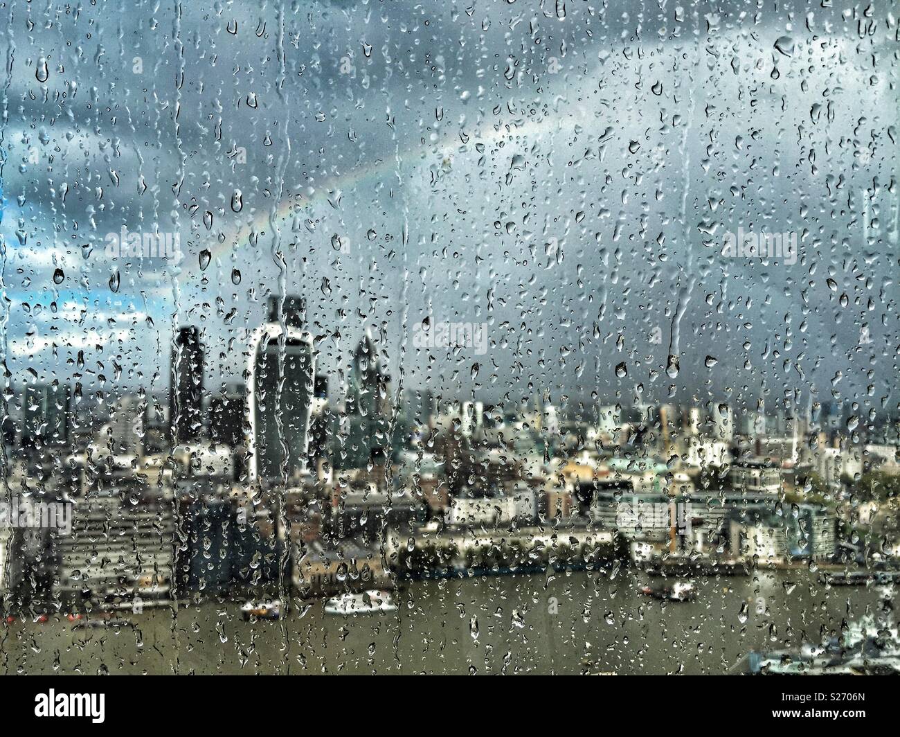 Rain on the window of The Shard, London, UK, looking across the Thames towards Fenchurch Street and over the City. A rainbow lights up the sky as the sun breaks through, lighting up the city below. Stock Photo
