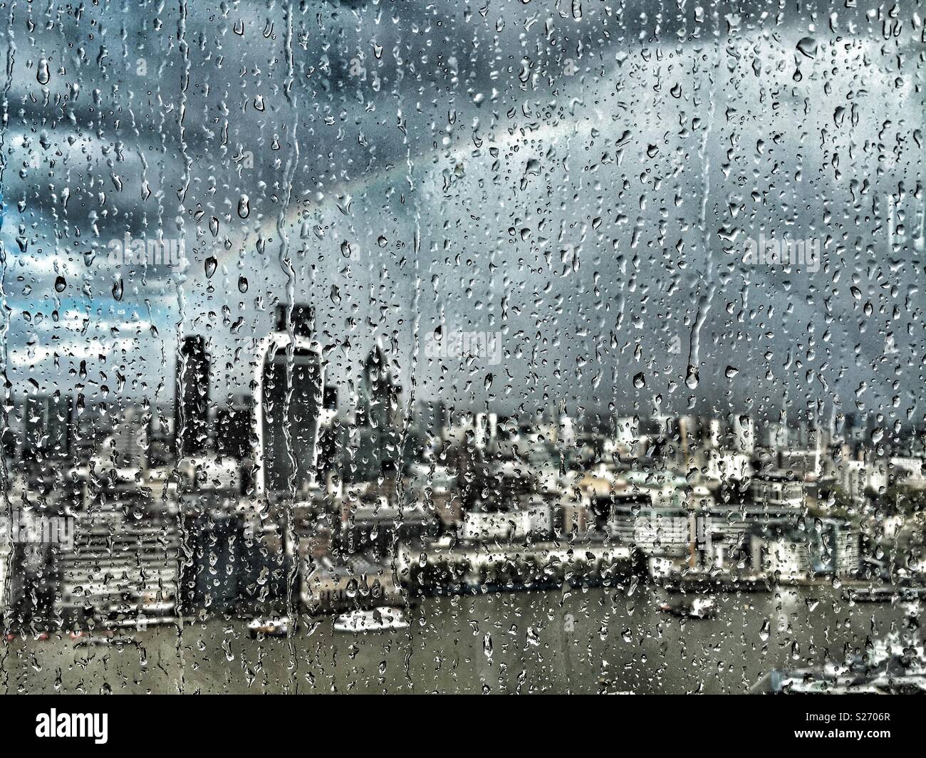 Rain on the window of The Shard, London, UK, looking across the Thames towards Fenchurch Street and over the City. A rainbow lights up the sky as the sun breaks through, lighting up the city below. Stock Photo