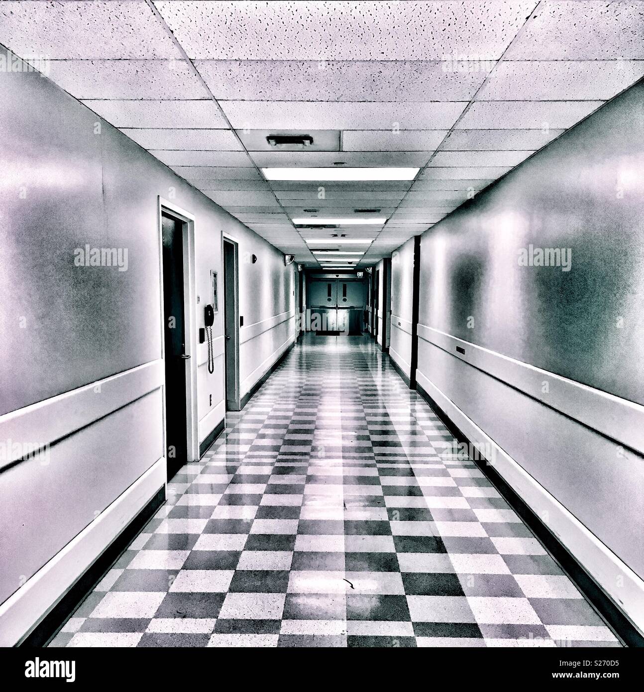 Creepy hospital hallway with checkered tile floors and swing doors Stock Photo