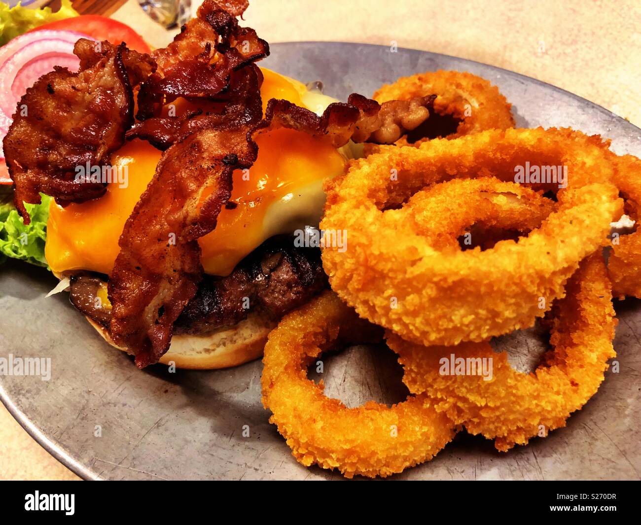 Half pound deluxe bacon cheeseburger with a side of onion rings on an iron platter. - Smartphone Captured Stock Image