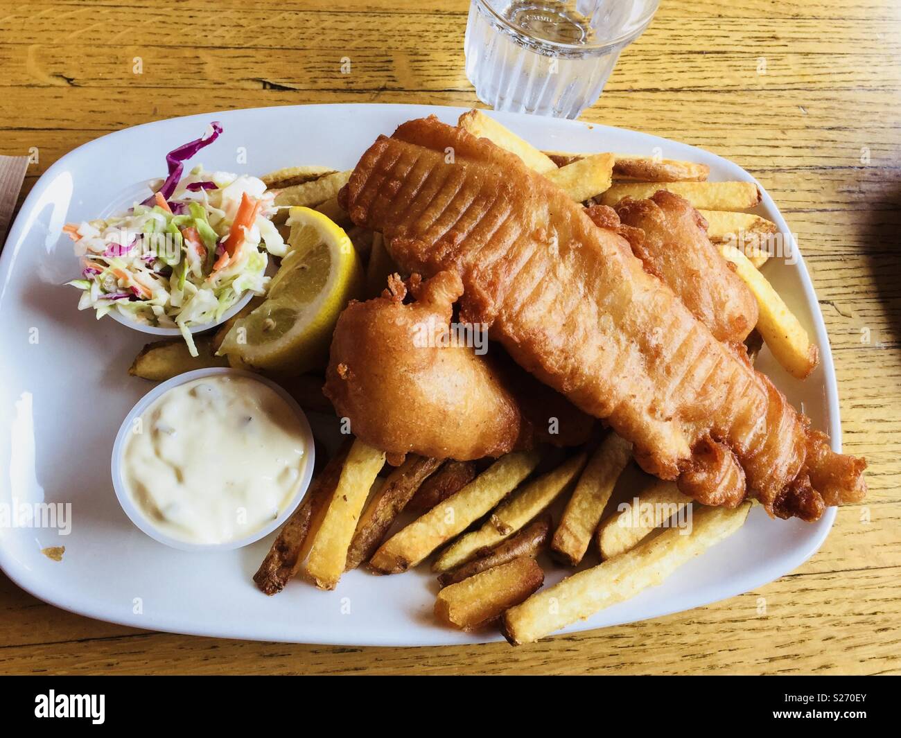 A plate of fish and chips with lemon wedge, tartar sauce and Cole slaw