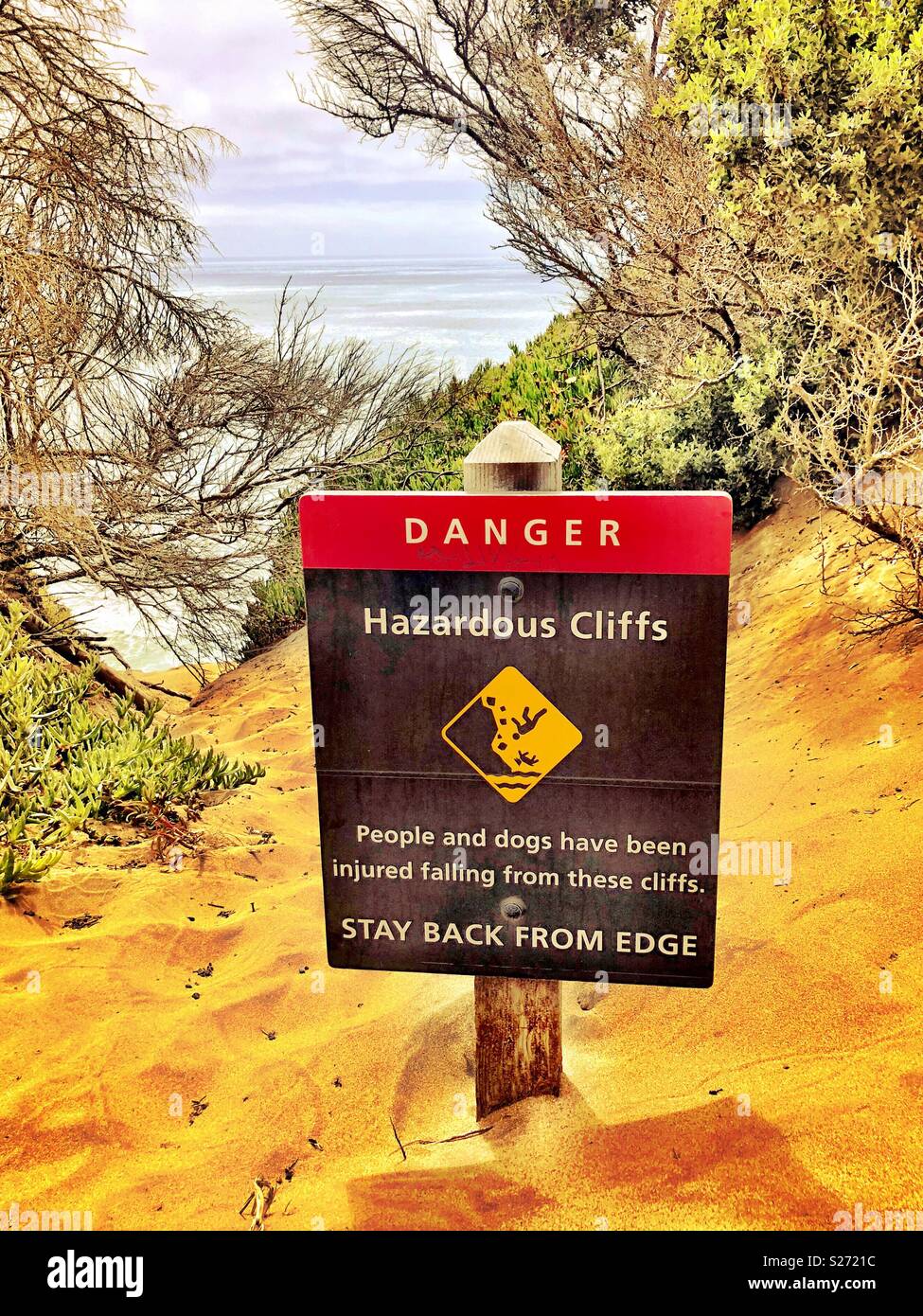 Dangerous falling hazard sign posted atop sandy coastal California cliff with lively colorful panoramic view. - Smartphone Captured Stock Image