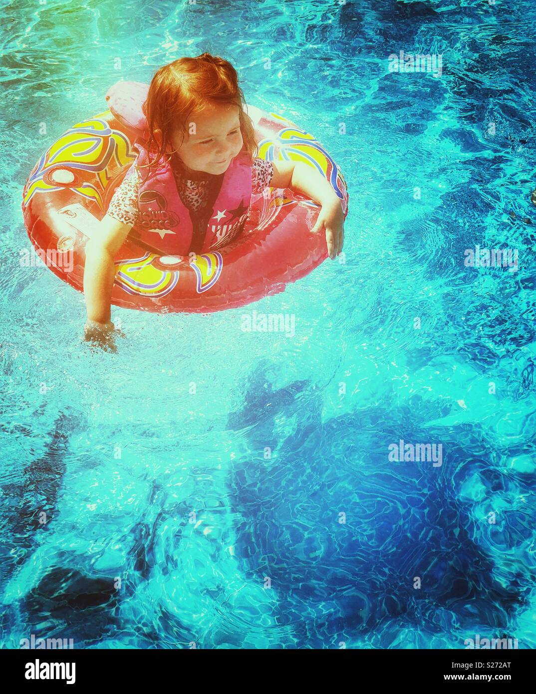 Toddler girl in a swimming pool with life vest and flotation ring on a