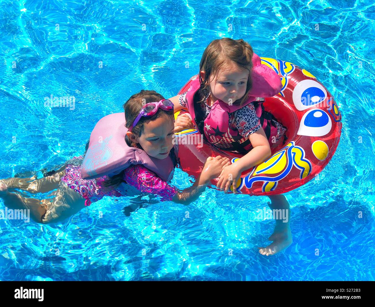 Two young girls swimming and playing together in a pool with life vests
