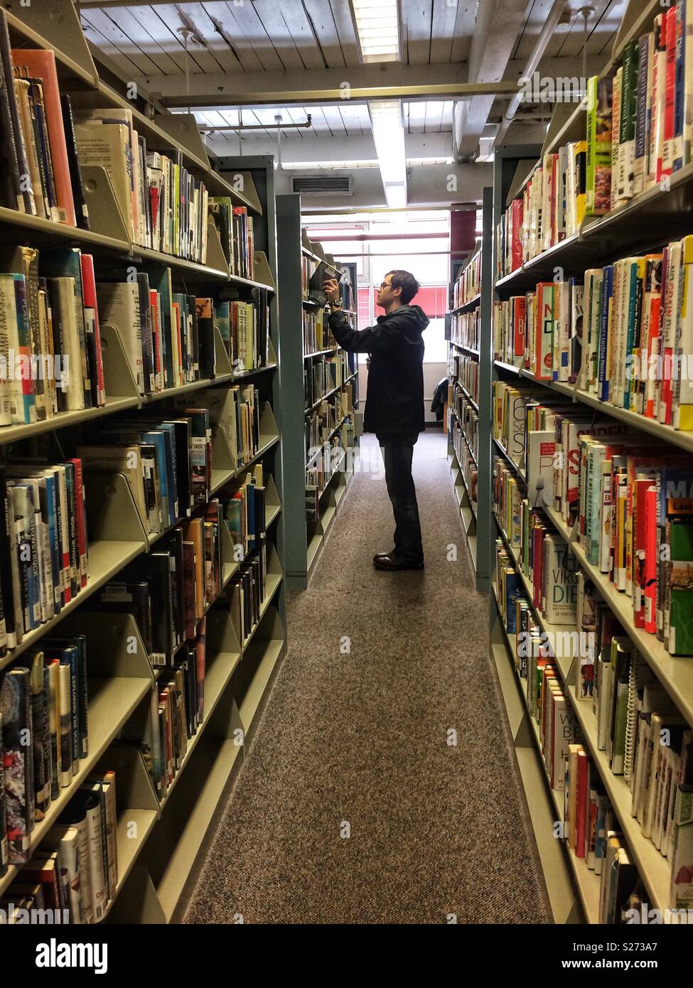 Man choosing a book from library bookshelves Stock Photo Alamy