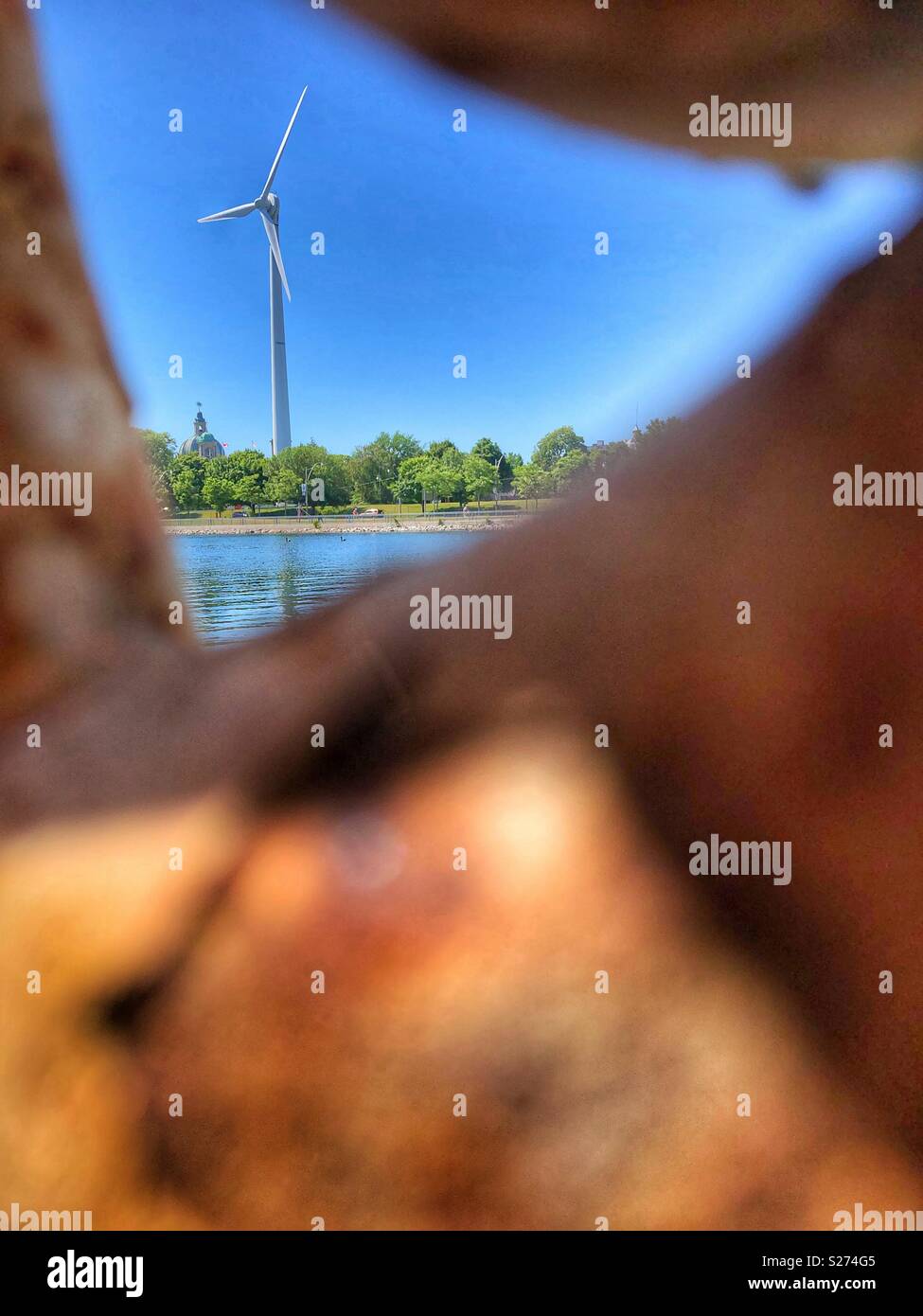 A framed view of a windmill through a rusted chain link. - Smartphone Captured Stock Image