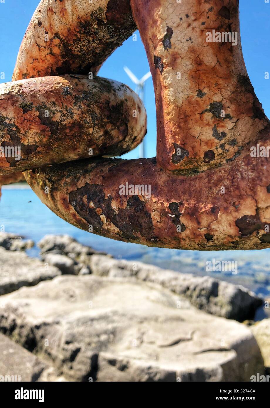 Looking through a rusted chain link along a rocky shoreline. - Smartphone Captured Stock Image