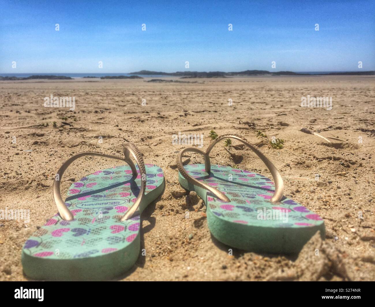 Flip flops large in foreground of beach scene, Rhosneigr, Anglesey, North Wales, UK - Smartphone Captured Stock Image