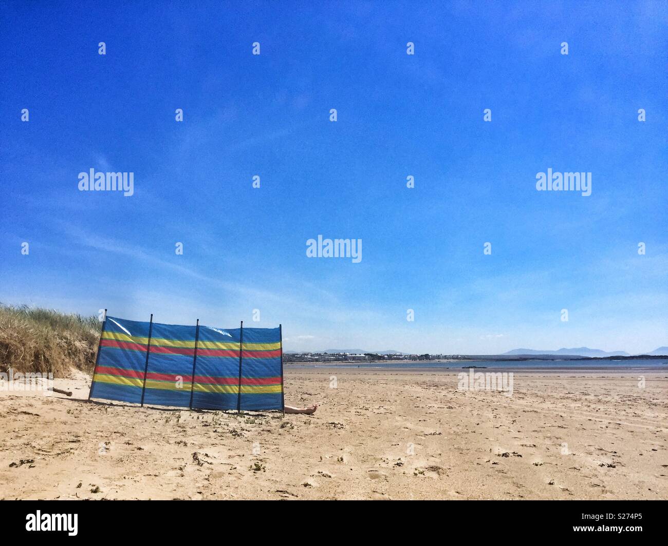 Feet sticking out from behind a striped multicoloured windbreaker on Cymyran beach, Rhosneigr, Anglesey, North Wales, UK - Smartphone Captured Stock Image