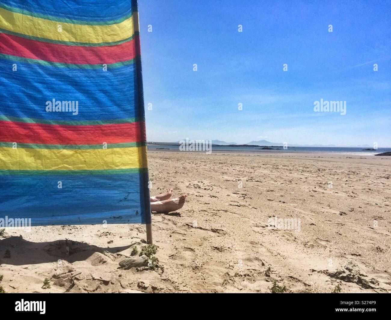 Feet sticking out from a windbreaker in Cymyran beach, Rhosneigr, Anglesey, North Wales, UK - Smartphone Captured Stock Image