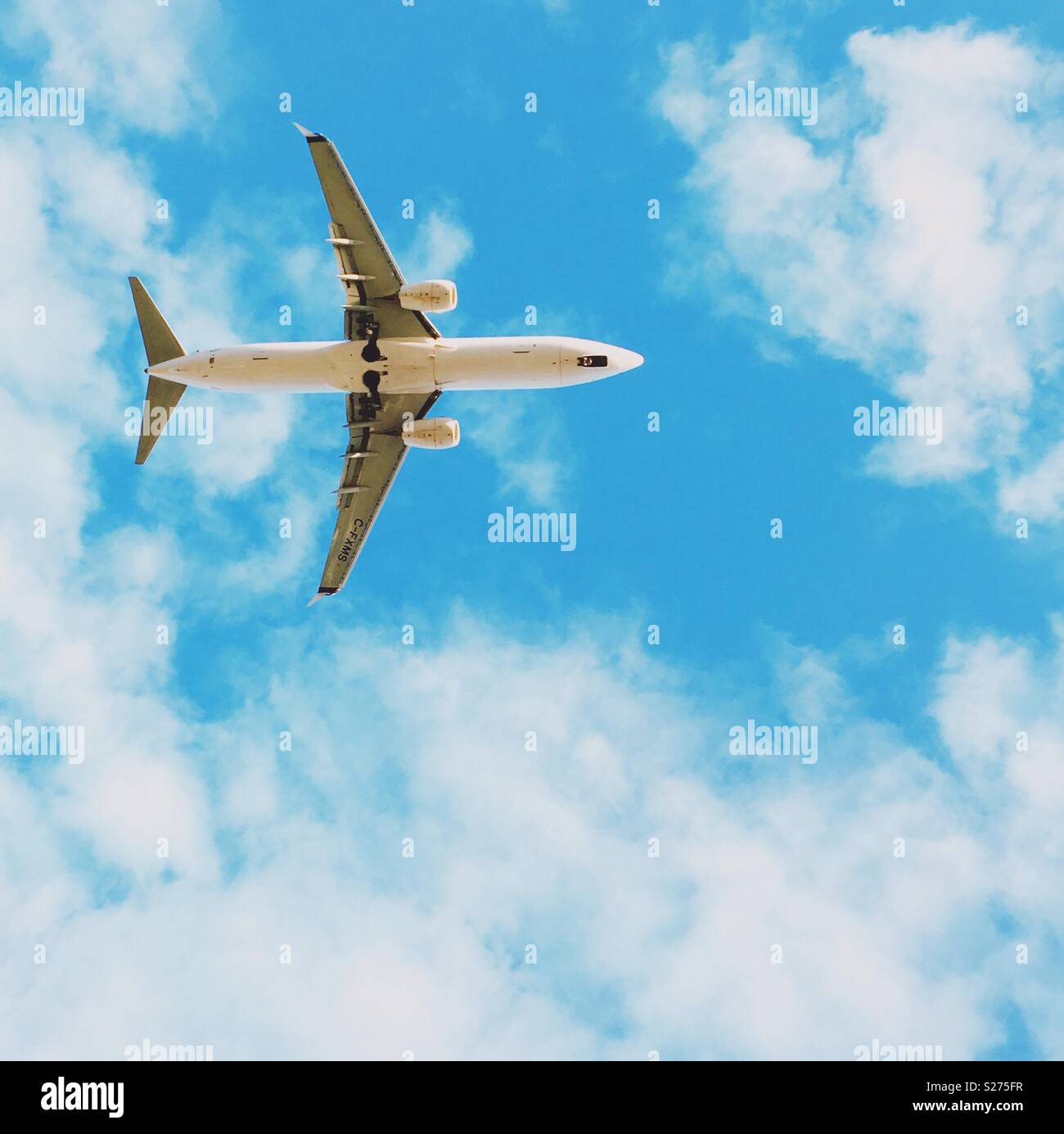 Airplane photographed from below as it approaches airport for landing, with blue sky and white clouds in the background. Square crop. Room for copy. - Smartphone Captured Stock Image