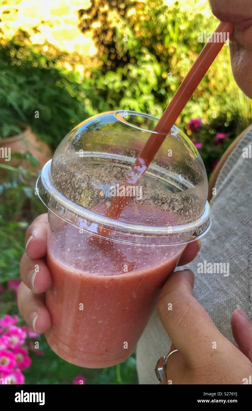 Millennial woman drinking a berry fruit smoothie outdoors on a hot summer day - Smartphone Captured Stock Image