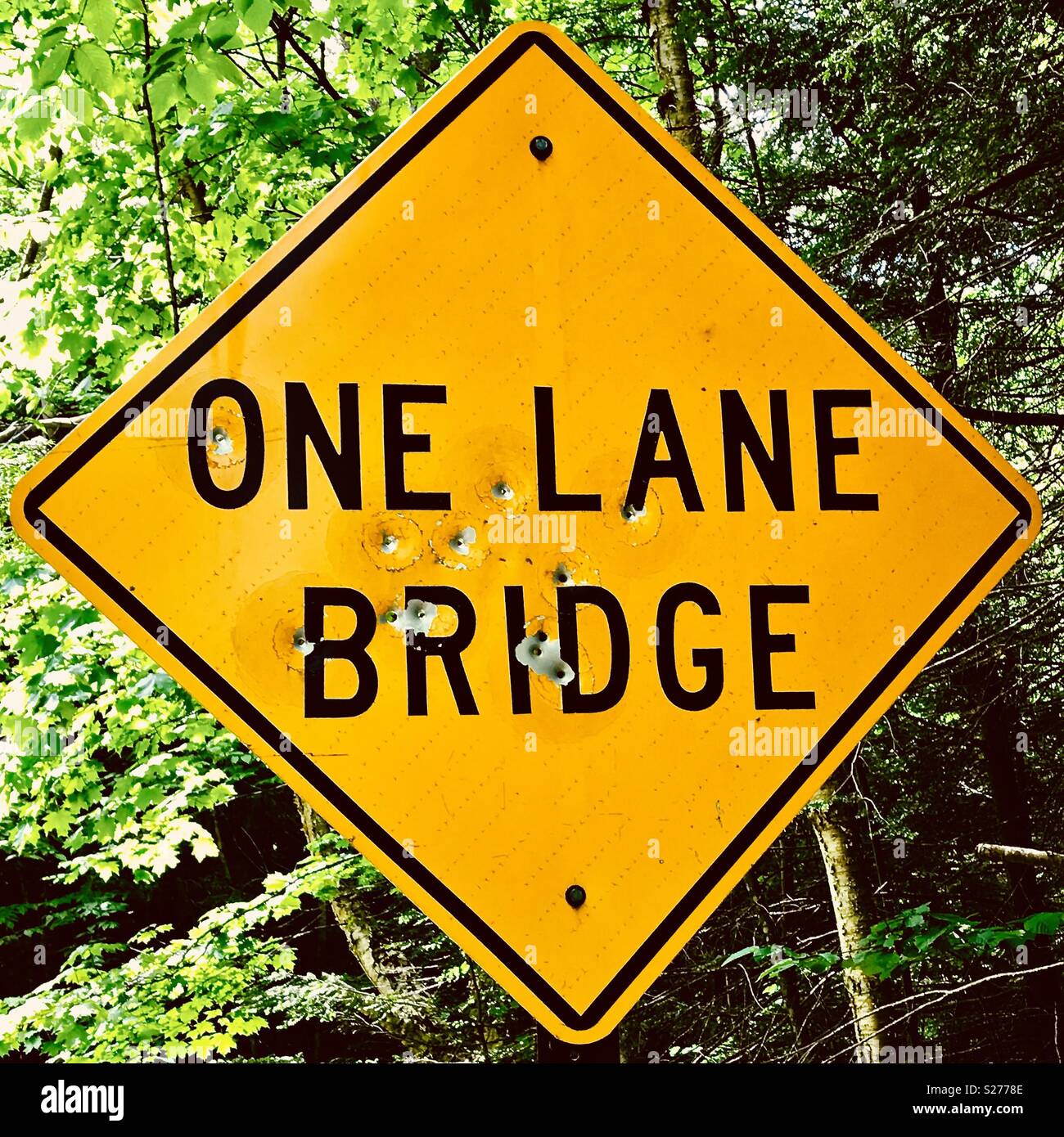 One lane bridge sign in the Adirondack wilderness with bullet holes from vandals. Stock Photo