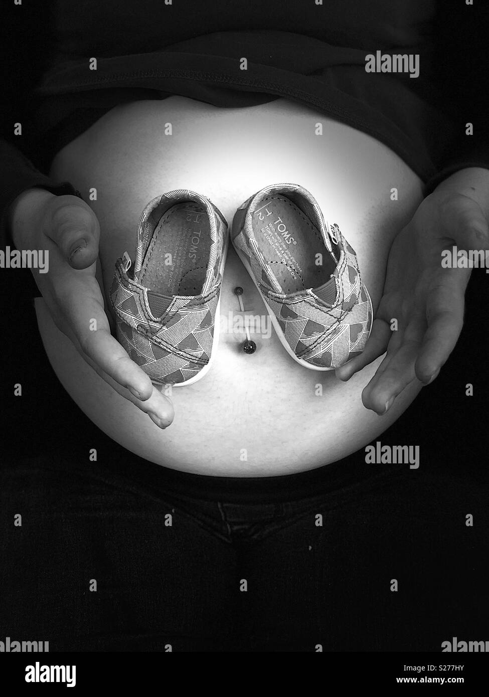 Baby shoes hold against pregnant woman’s stomach Stock Photo