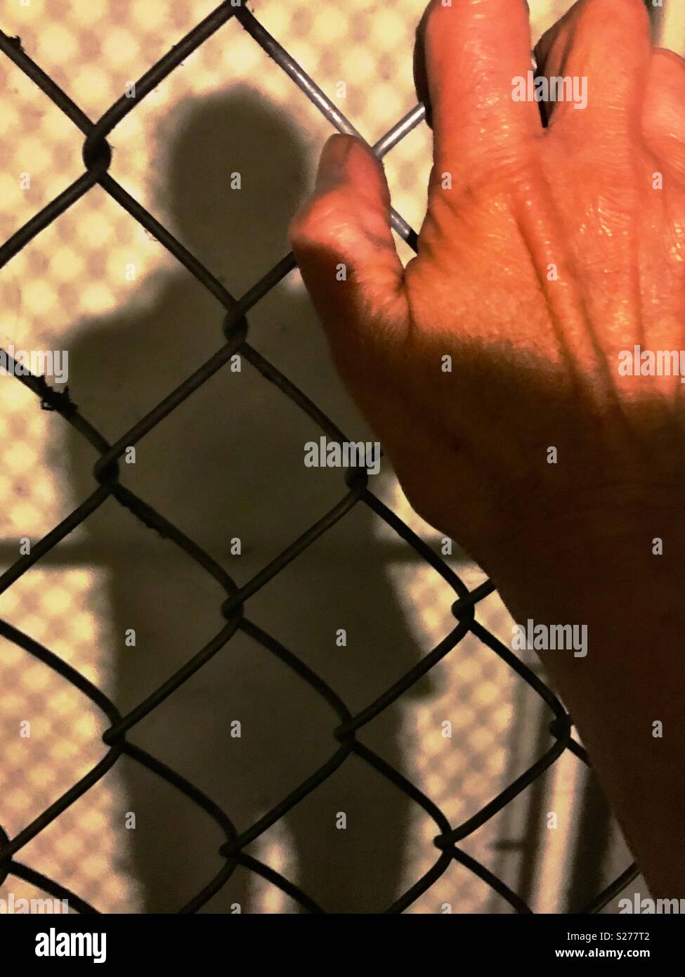 Man’s hand and shadow, with chain link fence Stock Photo