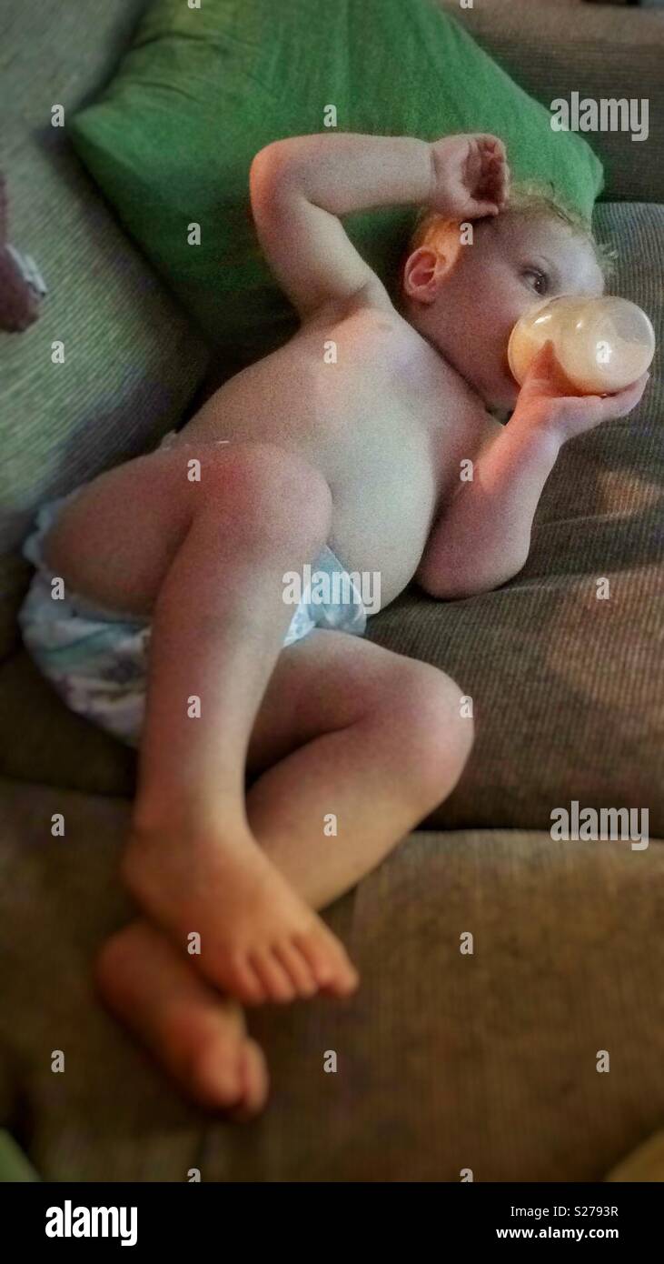 One year old baby boy drinking a bottle of milk on the sofa. - Smartphone Captured Stock Image