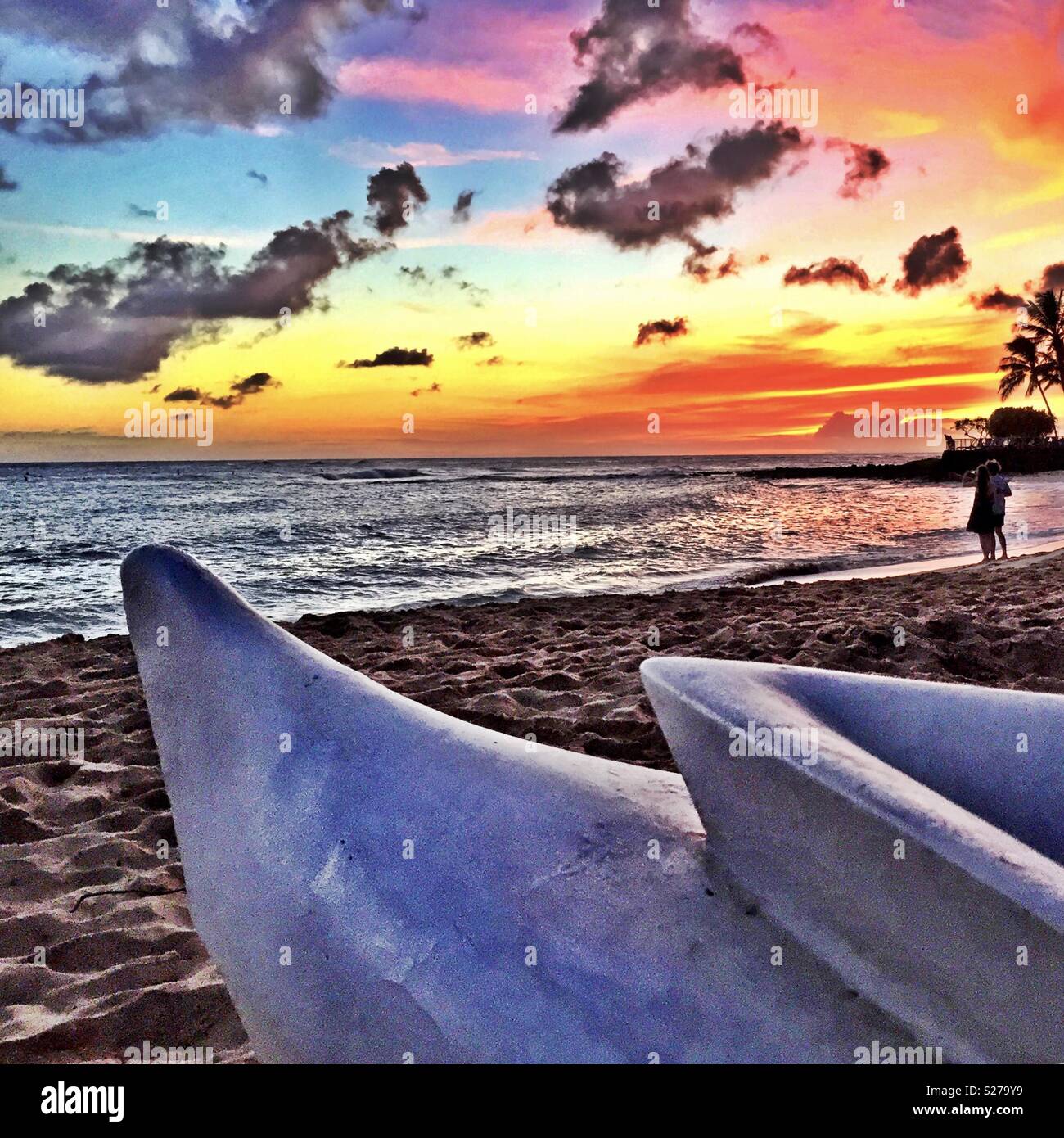 Couple beholds spectacular tropical island ocean sunset on the beach with outrigger canoe in the fore - Smartphone Captured Stock Image