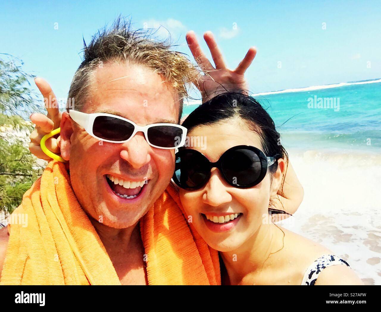 Turquoise reef and ocean waves behind smiling ecstatic couple having fun on a tropical island beach paradise - Smartphone Captured Stock Image