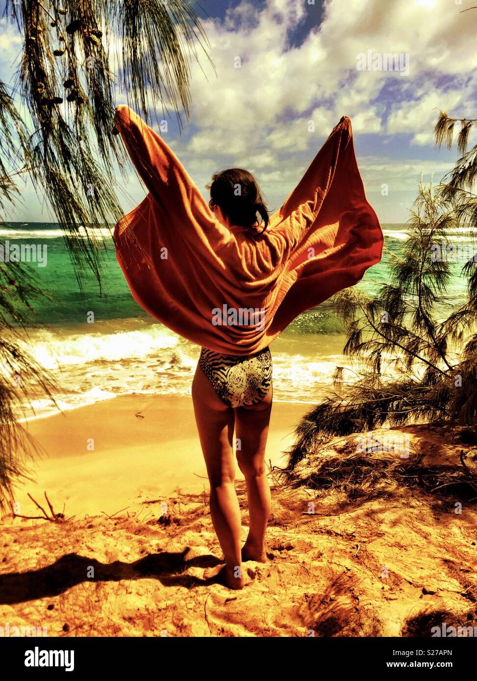 Young brunette woman in swimsuit drying off with orange towel at tropical island beach shore - Smartphone Captured Stock Image