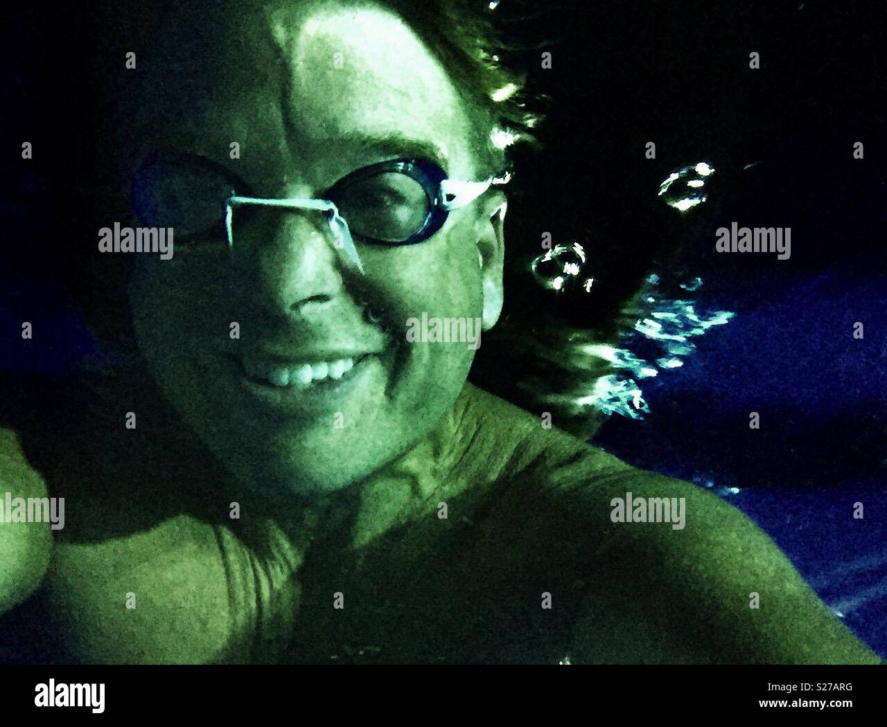 Gushing bubbles behind goggled face of submerged man in swimming pool at night - Smartphone Captured Stock Image