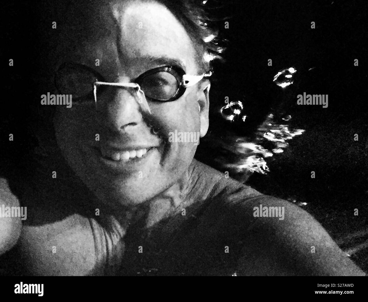 Smiling young male swimmer with goggles submerged under water in swimming pool with bubbles emanating from behind - Smartphone Captured Stock Image