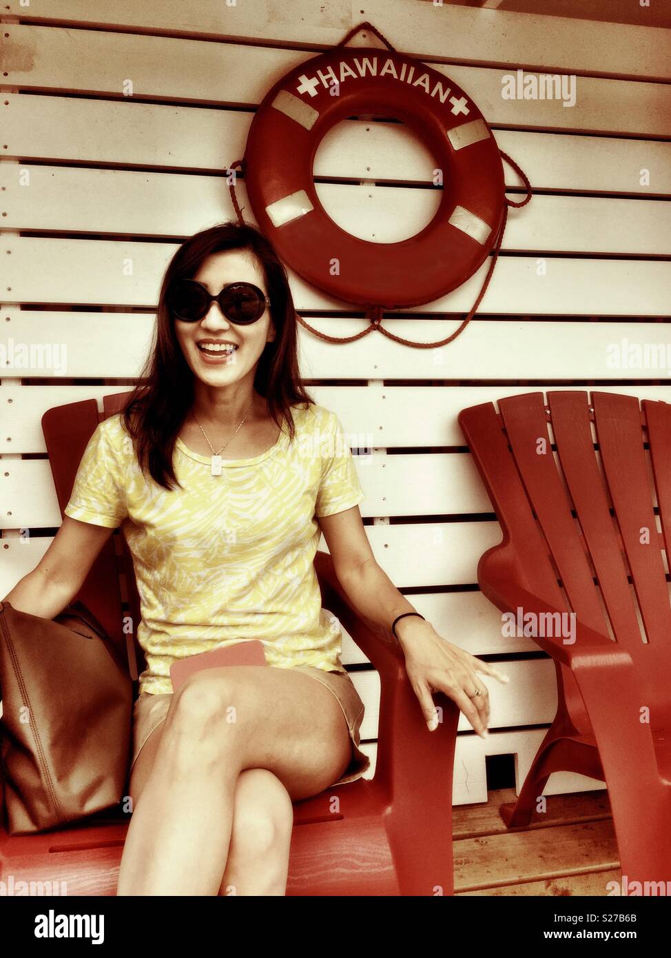Lovely beautiful young brunette woman with sunglasses and short shorts sitting on red Adirondack deck chair smiling Stock Photo Alamy