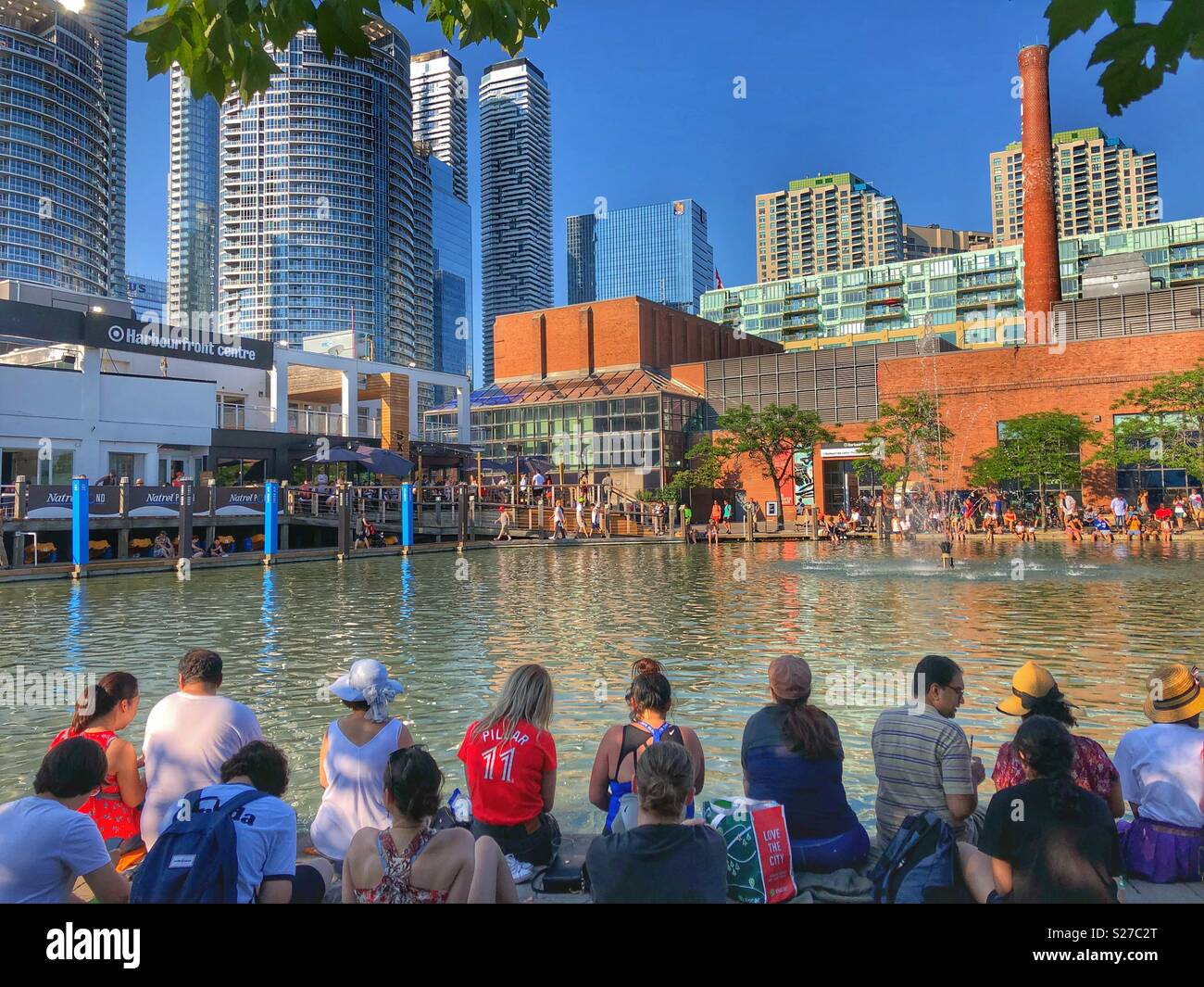 People sitting around the Natrel pond at Harbourfront Centre on a hot summer day in Toronto. - Smartphone Captured Stock Image