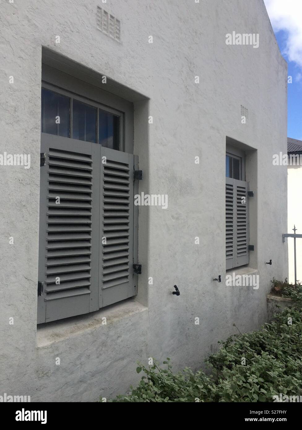 Front view of pale grey house with closed half shutters which are wooden and painted medium grey for exterior of residential dwelling in upmarket suburb - Smartphone Captured Stock Image