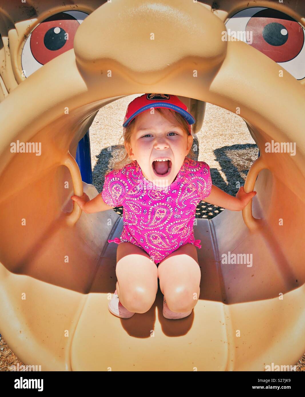 Five year old girl having fun and screaming inside a mouth open play structure at a public playground - Smartphone Captured Stock Image