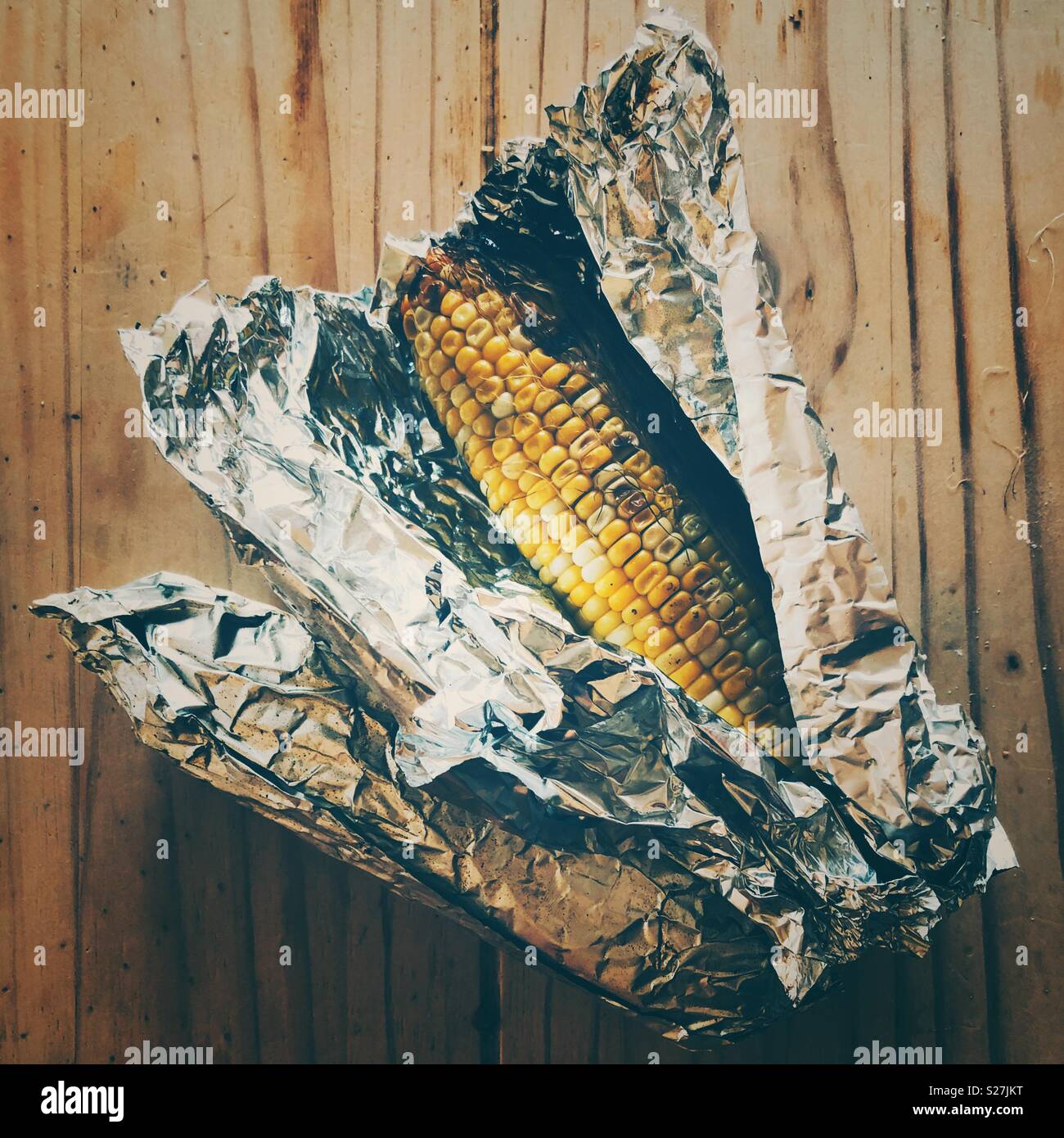 Two corn on the cobs that were just Barbecued wrapped in aluminum foil with one partially unwrapped Stock Photo