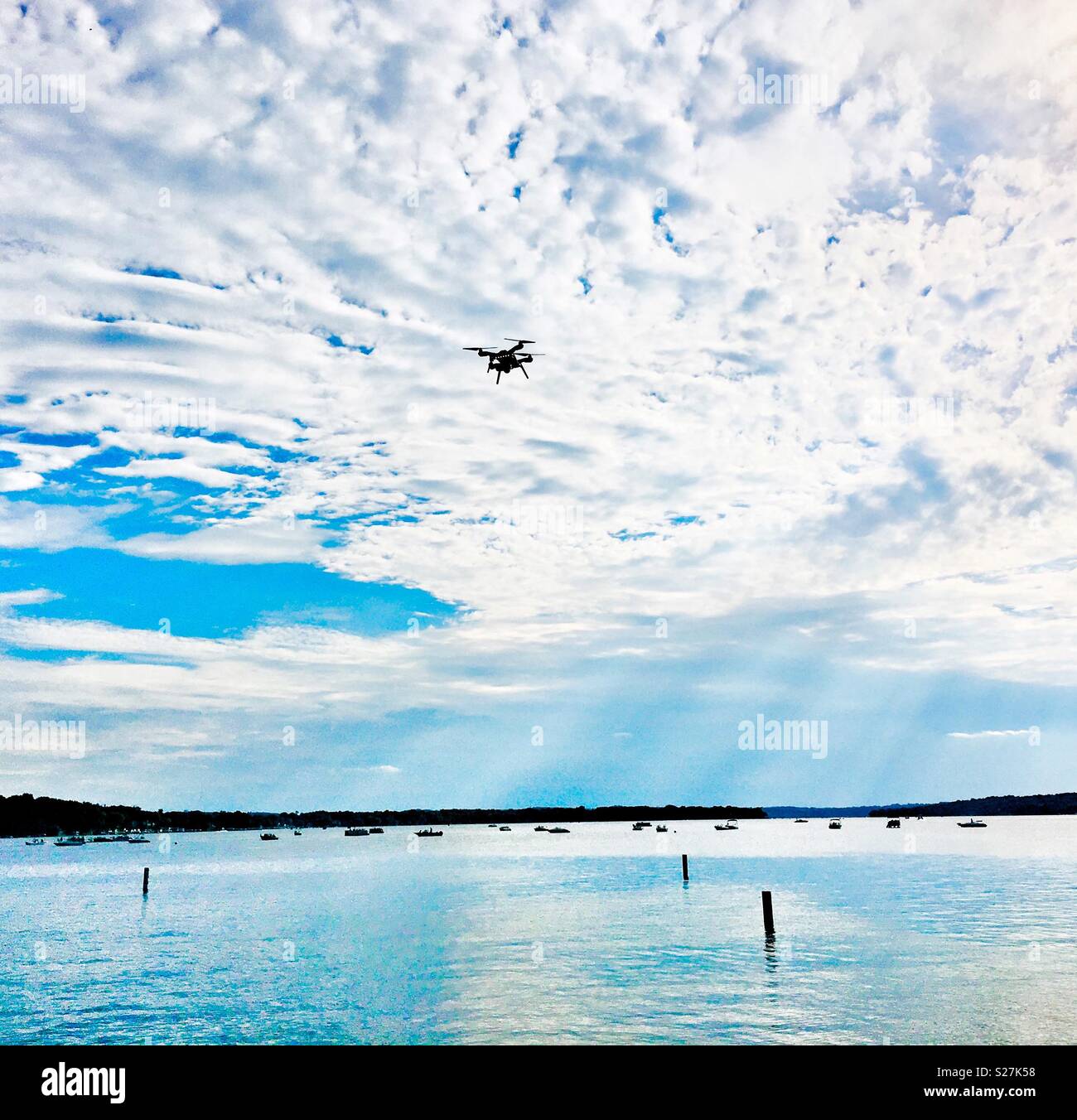 Drone flying against clouds over lake with boats and blue sky - Smartphone Captured Stock Image