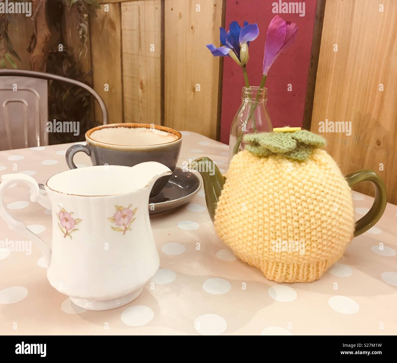 Time for tea. Teapot and tea cosy with milk jug and tea cup on spotted tablecloth with flowers. Stock Photo