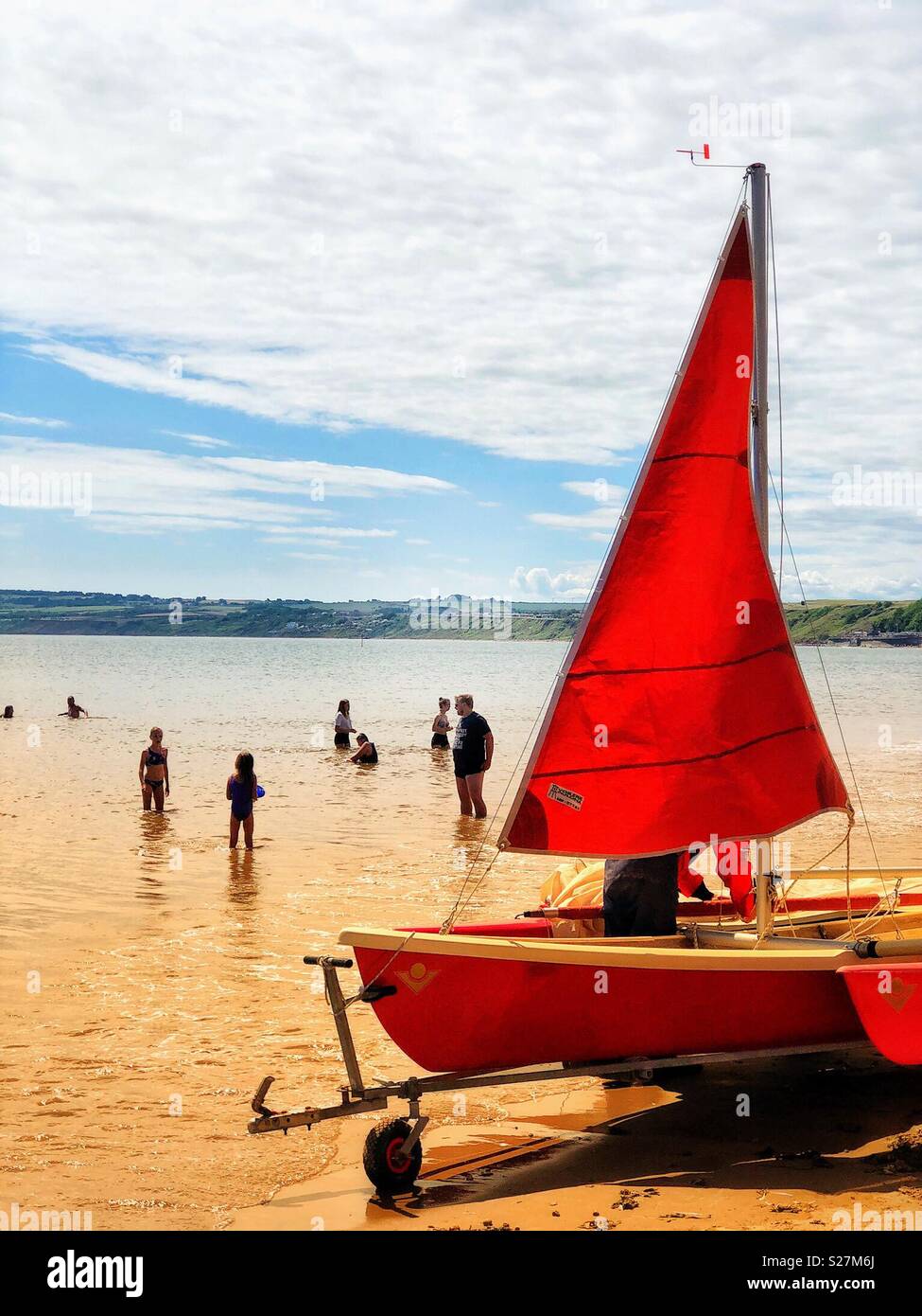 Red sailing dinghy with red sail being readied for launch into the sea at Filey, North Yorkshire, UK - Smartphone Captured Stock Image