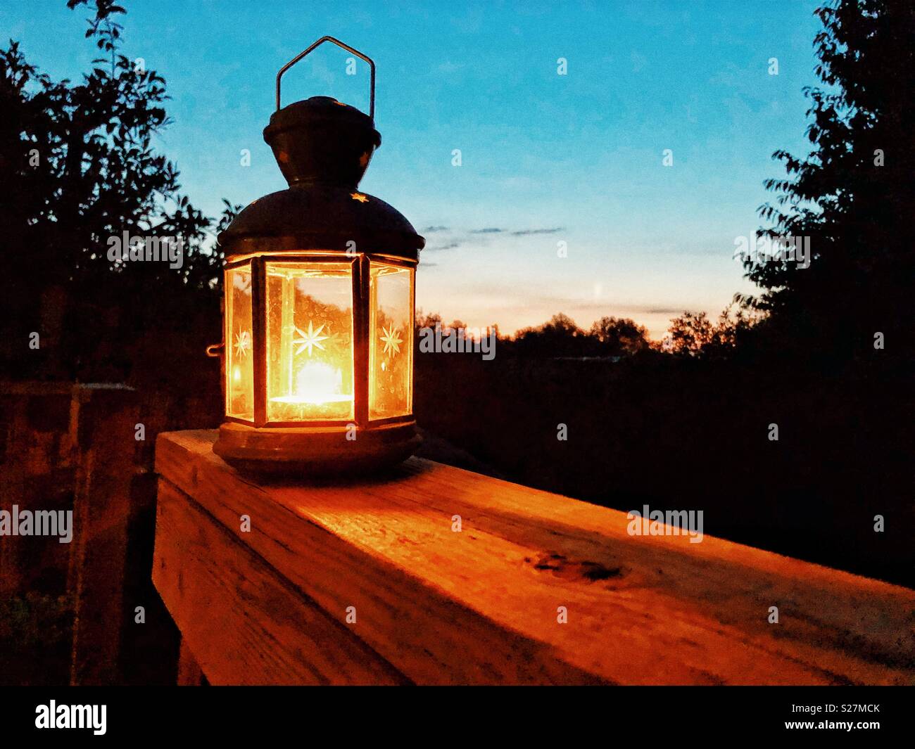 Candle lamp sitting on a wooden decking rail at sunset on a hot summer night. - Smartphone Captured Stock Image