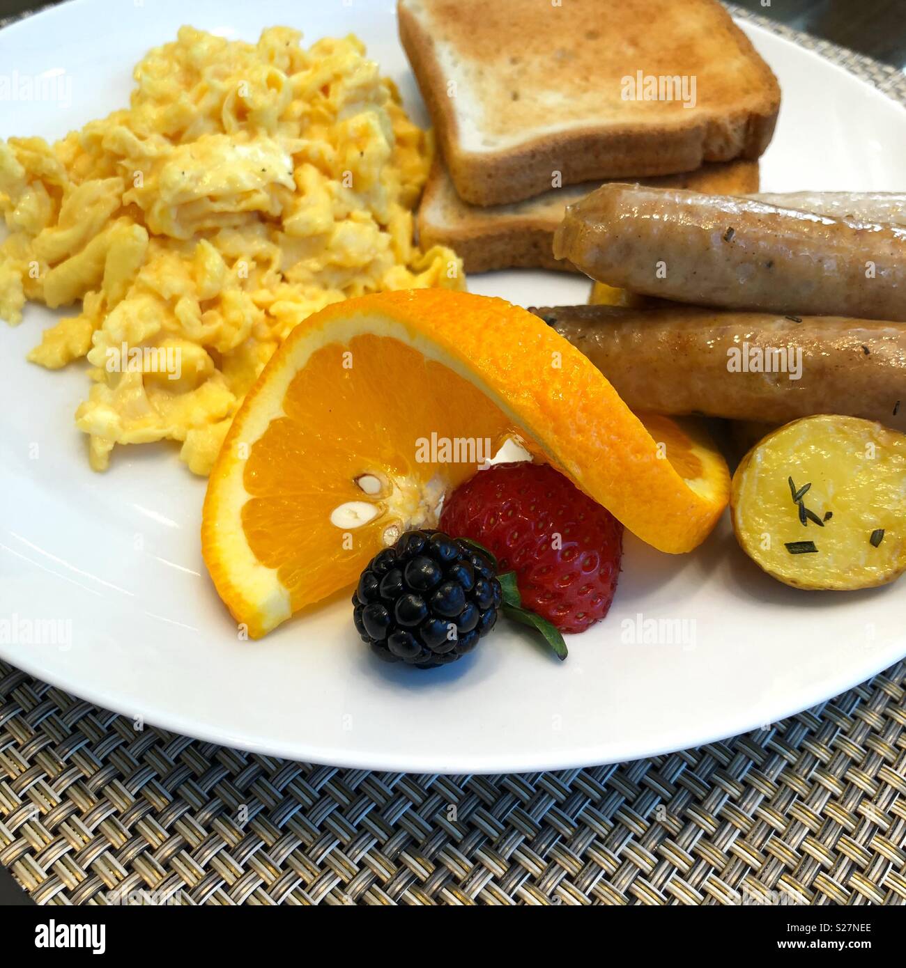 A beautifully plated breakfast of scrambled eggs, toast, potatoes, sausage and fruit garnish Stock Photo