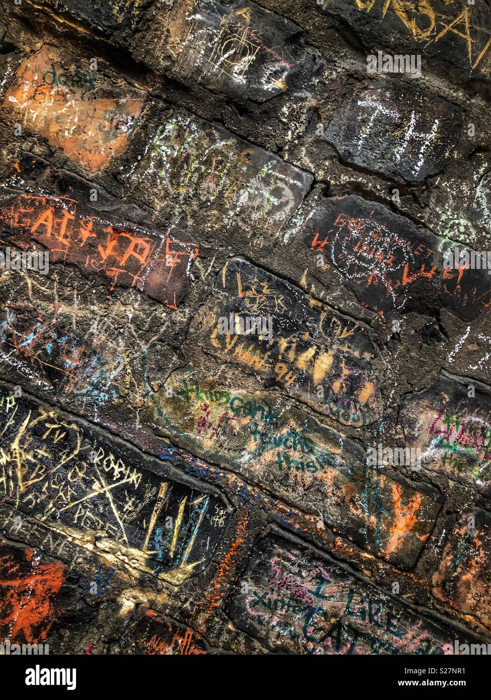 Many names and dates written on a black brick wall in chalk - Smartphone Captured Stock Image