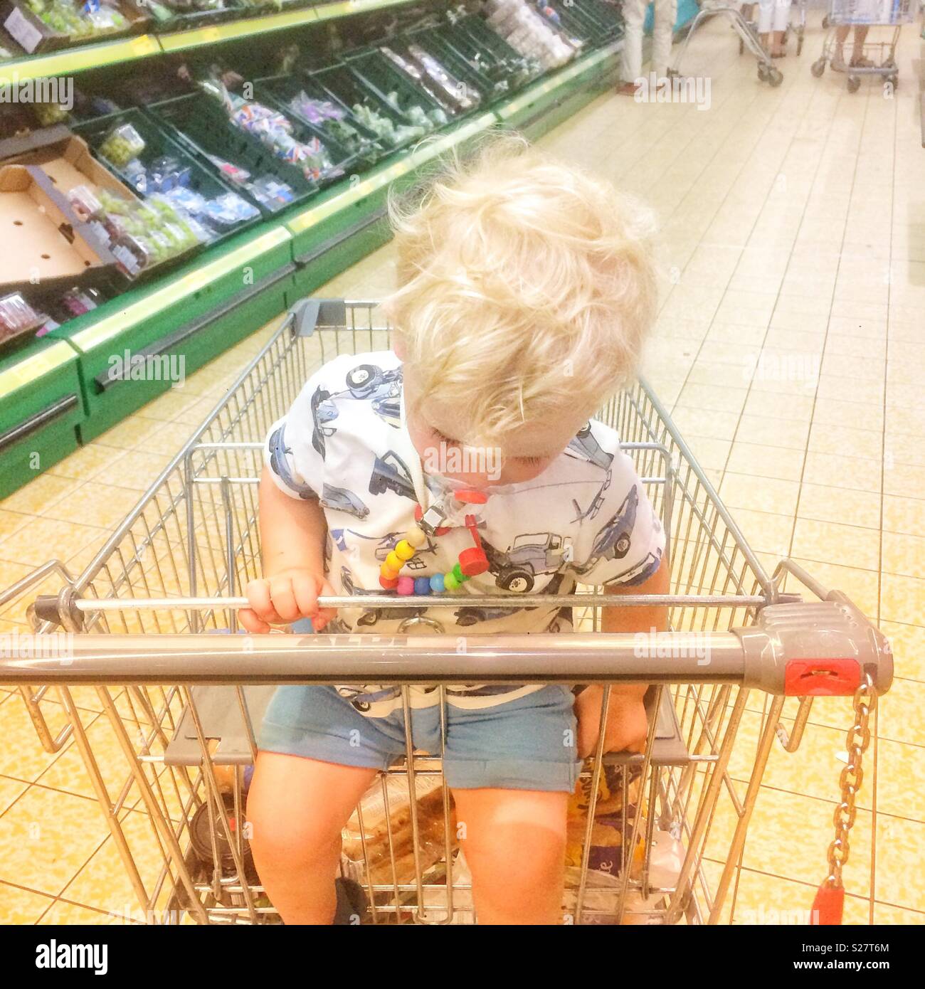 Two year old baby boy falling asleep in a supermarket shopping trolley,Hampshire, England, United Kingdom. - Smartphone Captured Stock Image